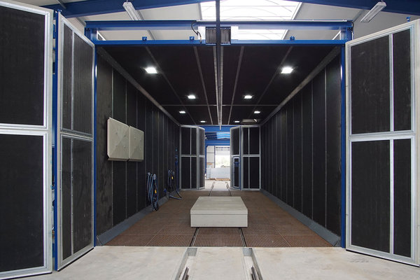 Zu sehen ist eine 10 m lange Strahlkabine mit beidseitigen Falttoren. An der Decke befindet sich eine Einfahrschiene. Bauteile können auf dem im Boden integrierten Schienensystem transportiert werden.